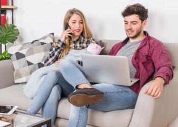 Paar sitzt auf der Couch, Frau telefoniert und der Mann surft am Laptop im Internet