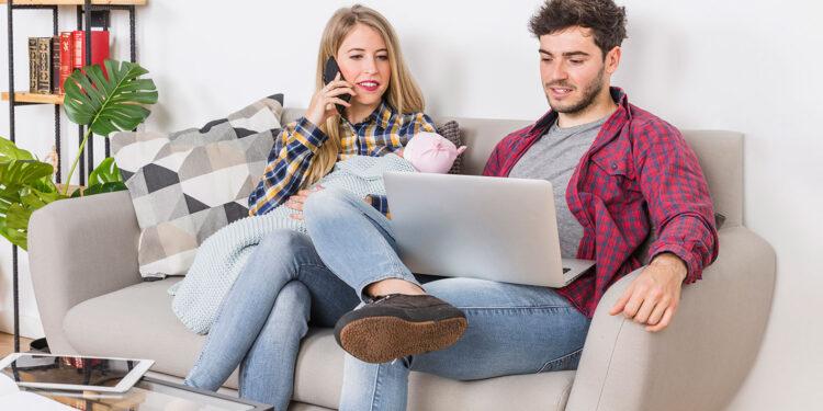 Paar sitzt auf der Couch, Frau telefoniert und der Mann surft am Laptop im Internet