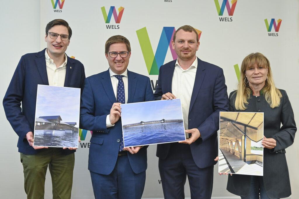 V.l. Mobilitätsstadtrat Stefan Ganzert (Wels), Bgm. Dr. Andreas Rabl (Wels), Mag. Johann Knoll sowie Vbgm. Heidi Strauss (Marchtrenk) präsentieren den Entwurf für die Geh- und Radwegbrücke über die Traun. Nicht auf dem Bild ist Bürgermeister Andreas Stockinger (Thalheim).